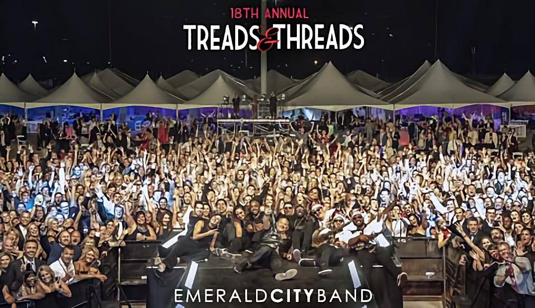 Large crowd at a nighttime outdoor event with tents and stage lighting.