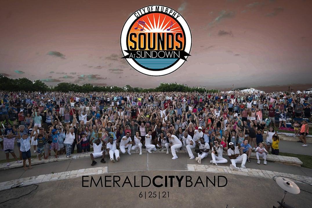 Large outdoor concert crowd with performers in white on stage at sunset.