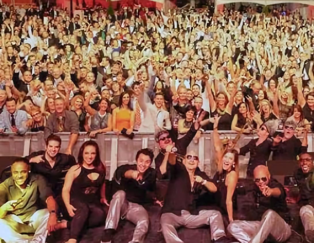 Members of Emerald City Band sitting on stage in front of a large crowd