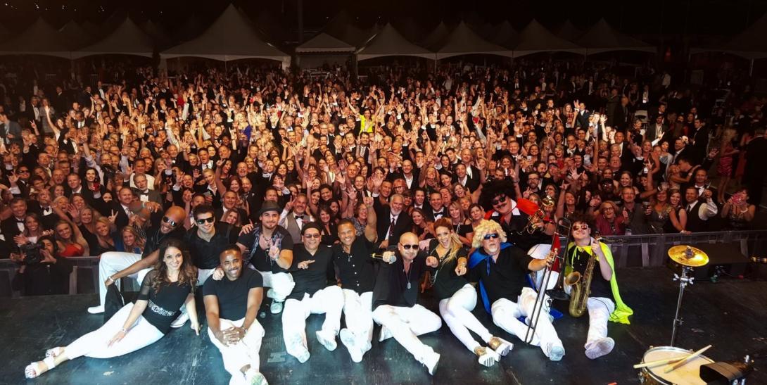 Members of Emerald City Band sitting on stage with a large crowd behind them
