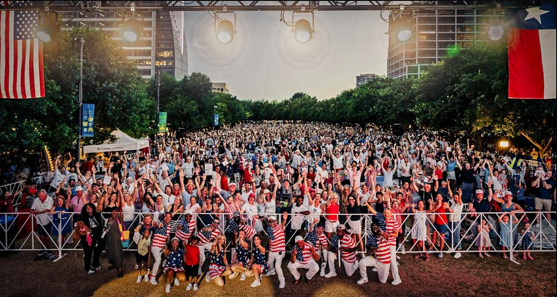 Large crowd at an outdoor event, many people wearing red, white, and blue, flags displayed.